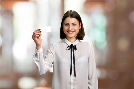 Young business lady showing blank card. Beautiful young woman in formal blouse holding business card on blurred background.の写真素材