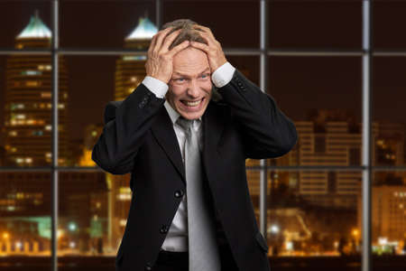 Portrait of desperate mature businessman. Depressed male executive holding hands on head in...