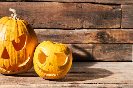 Two Halloween pumpkins on rustic wood background. Carved orange pumpkins and sunlight. Halloween pumpkins carving ideas.の写真素材