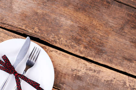 Halloween table setting on rustic wooden table. Plate with cutlery and black dotted ribbon on old...