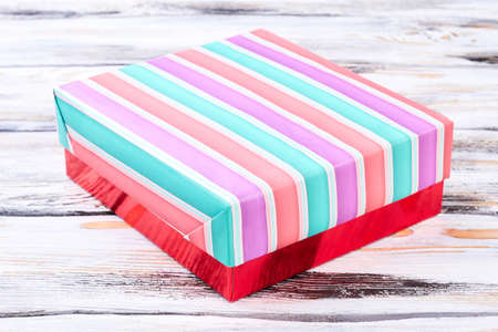 Multicolored striped gift box. Colorful striped closed gift box on white wooden background. New Year...