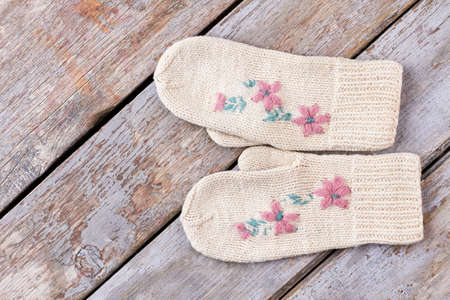 Pair of female warm woolen mittens. White embroidered knitted gloves for ladies on rustic wooden background. Beautiful handmade Christmas gift.の写真素材