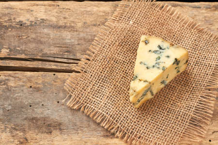 Piece of French Roquefort cheese on rustic background. Blue cheese on hessian cloth. Tasty milk...