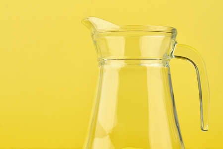 Clean glass jug on yellow background. Blank transparent pitcher on colored background, cropped image.の写真素材
