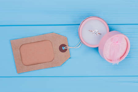 Wedding ring in round box and blank tag. Copyspace. Blue wood background.の写真素材