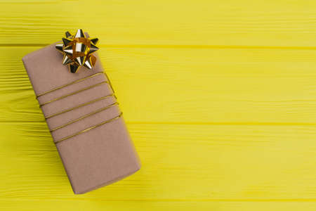 Gift box wrapped in cardboard paper. Copyspace. Yellow wood background.の写真素材