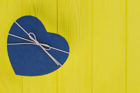 Blue gift box with a heart shape. Yellow wood background. Top view.の写真素材
