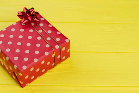 Wrapped box in dotted paper. Red bow. Yellow wood background.の写真素材