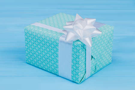 Green patterned gift box with white ribbon. Blue wooden table background.の写真素材