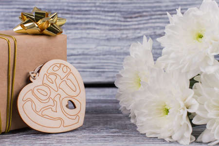 Gift, flowers and wooden heart. Box with goden bow, heart with inscription love you and white chrysanthemums. Valentines Day background.の写真素材