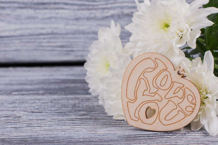 Bouquet of flowers and wooden heart. White chrysanthemums and carved wooden ornament for Valentines holiday. Valentines Day wooden background.の写真素材
