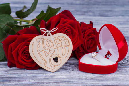 Valentines holiday background. Romantic composition with red roses, wooden heart and golden ring in...