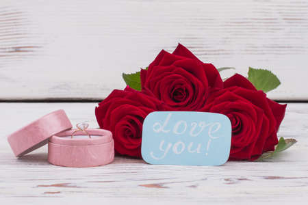 Wedding ring in box and red roses. Engagement ring, blooming flowers and card with handwritten...