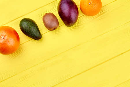 Assortment of exotic fruits including grapefruit, kiwi, mango and orange on yellow wooden...