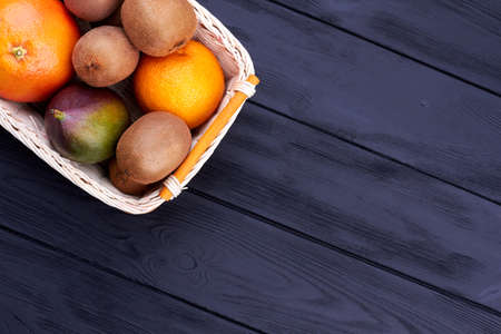 Fresh kiwi fruit, grapefruit, orange and mango in woven basket on wooden background with text space.