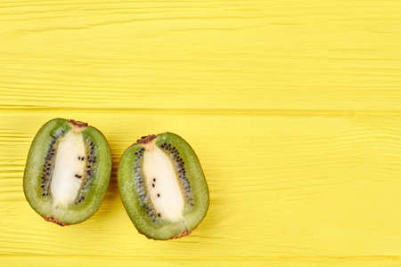 Fresh organic kiwi sliced in two parts on yellow wooden background with text space.