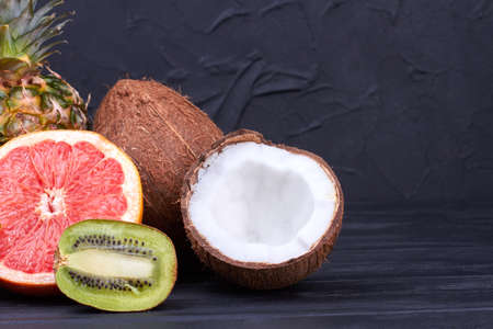Mix of exotic fruits on black background. Half of grapefruit, kiwi fruit and coconut on dark...