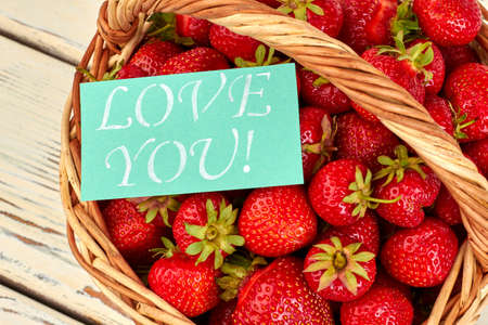 Close up juicy strawberries in basket. Fresh delicious strawberries and card with text love you.の写真素材