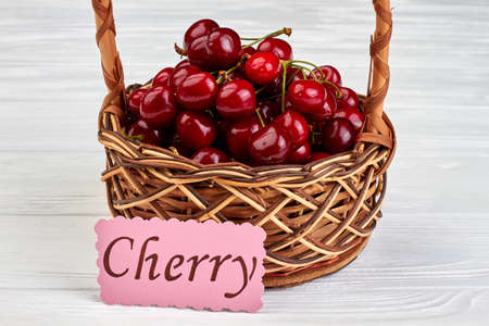 Sweet organic cherries in wicker basket on white wooden background.の写真素材