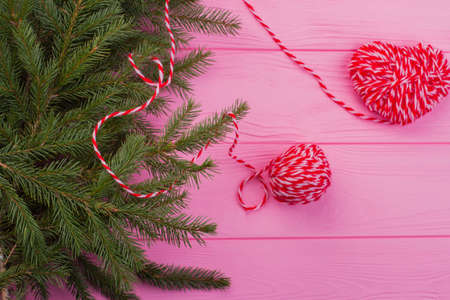 Christmas composition on pink wooden background. Fresh fir tree branches and red knitted heart....