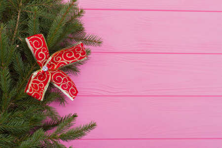 Left border of fresh fir tree branches. Spruce branches with red bow on wooden background, copy...
