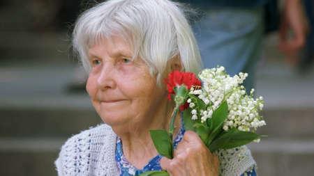 09.05.2018 - Kyiv, Ukraine. Close up old wrinkled woman holding fresh flowers. Face of senior grandmother.のeditorial素材