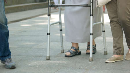 Senior woman walking with metal walker outdoors. Elderly disabled woman using a walking frame on the...