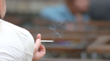 Burning cigarette in female hand. Close up female person is smoking, rear view. Nicotine addiction concept.の写真素材