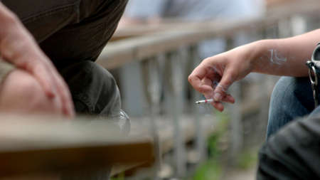 Young person with burning cigarette outdoors. Cigarette in female hand. Risks of smoking.
