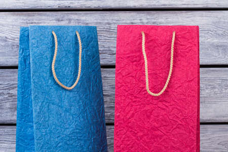 Two colorful shopping bags from crumpled paper. Beautiful design gift bags on wooden background. Sale, consumerism, advertisement and retail.の写真素材