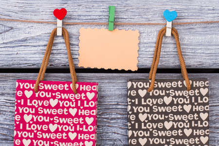 Valentine holiday gift bags. Shopping bags with I love you printing and blank paper card on wooden background. Holiday shopping concept.の写真素材