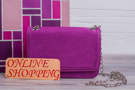 Stylish female pouch on wooden background. Pink leather handbag and card with inscription online...