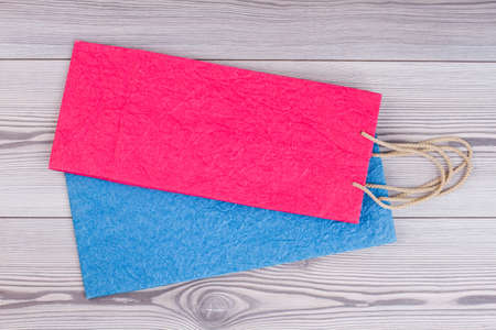 Flat lay colorful paper bags. Pink and blue shopping bags with handles on wooden background.