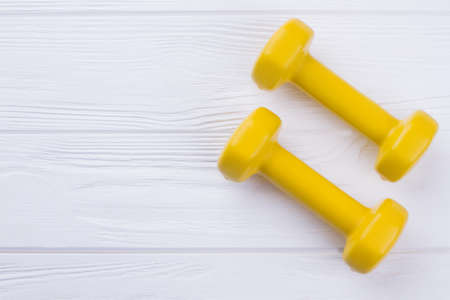 Two yellow dumbbells on wooden background. Pair of dumbbells with copy space. Diet and fitness concept.の写真素材