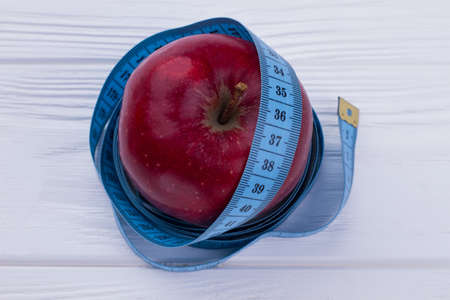 Healthy nutrition concept. Tape measure wrapped around red apple. Slimming diet and health care.