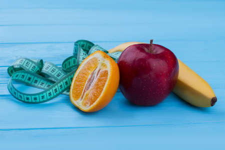 Healthy lifestyle and slimming concept. Measuring tape, banana, apple and orange fruit on blue...