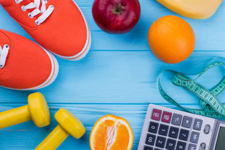 Concept of healthy life, sport and diet. Sport shoes, dumbbells, fruits, measuring tape, calculator...