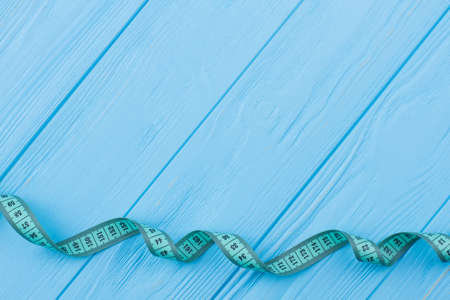 Tape measure on color wooden background. Measuring tape on blue surface with space for text. Dieting...