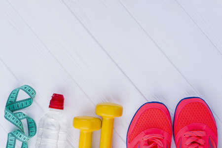 Fitness equipment on white background. Sport shoes, dumbbells, bottle of water and measuring tape...