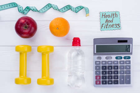 Dieting and fitness concept. Measuring tape, fruits, dumbbells, bottle of water and calculator....