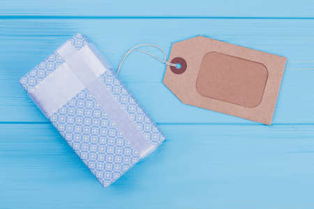 Patterned blue gift box and label tag. Blue wooden background.