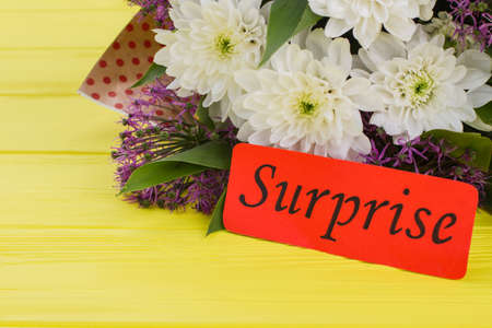 White daisy flowers bouquet and surprise word. Yellow wood background.