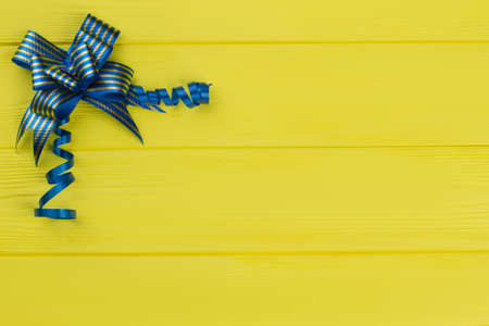 Blue Christmas or birthday gift ribbon bow. Copyspace, free space for text. Yellow wood background.