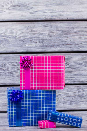 Gift boxes wrapped in blue and pink paper. Colored gift boxes with bow on wooden background....