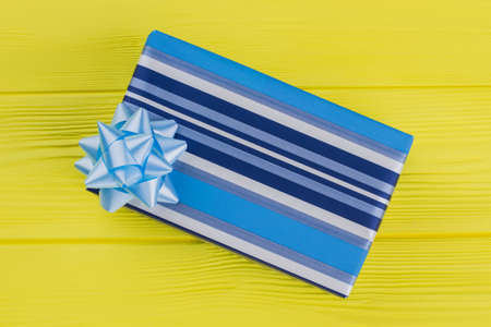 Blue striped gift box on yellow wood. Close up, top view.