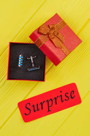 Steel cylindrical stud buttons in red gift box. Surprise concept. Yellow wood background.の写真素材