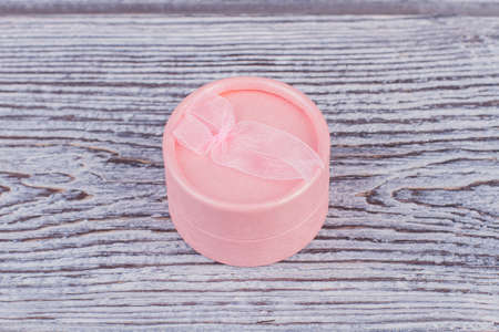 Pink jewelry box with bow ribbon. Beautiful round jewelry gift box on wooden background.