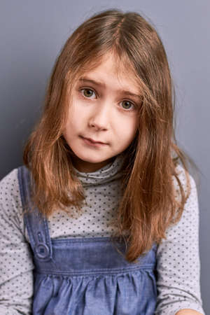 Upset brown hair little girl. Portrait of sad little beautiful girl isolated on grey background....