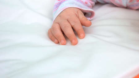 Beautiful tiny hand of infant girl. Infant kid on white blanket, cropped image. Beauty and softness...