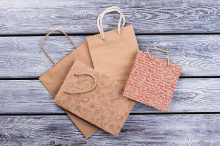 Kraft paper shopping bags on wooden background. Four brown carrier paper bags with handles, top...